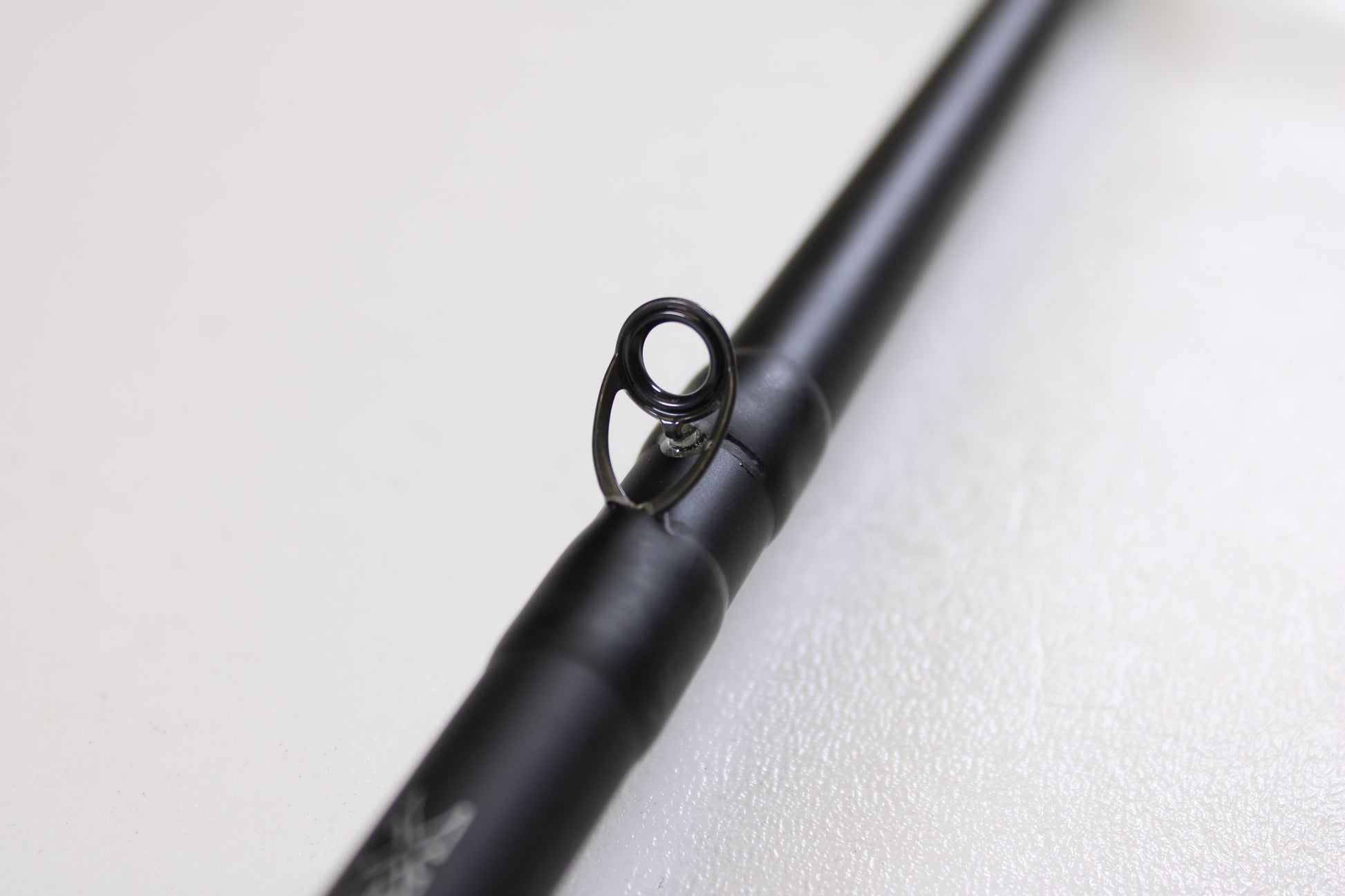 A close-up of the Daiwa Kage KAG761HRB-G Deep Crank 7'6" Heavy used casting rod in excellent condition, focusing on a single line guide against a blurred white background—ideal for anglers considering gear trade-ins.