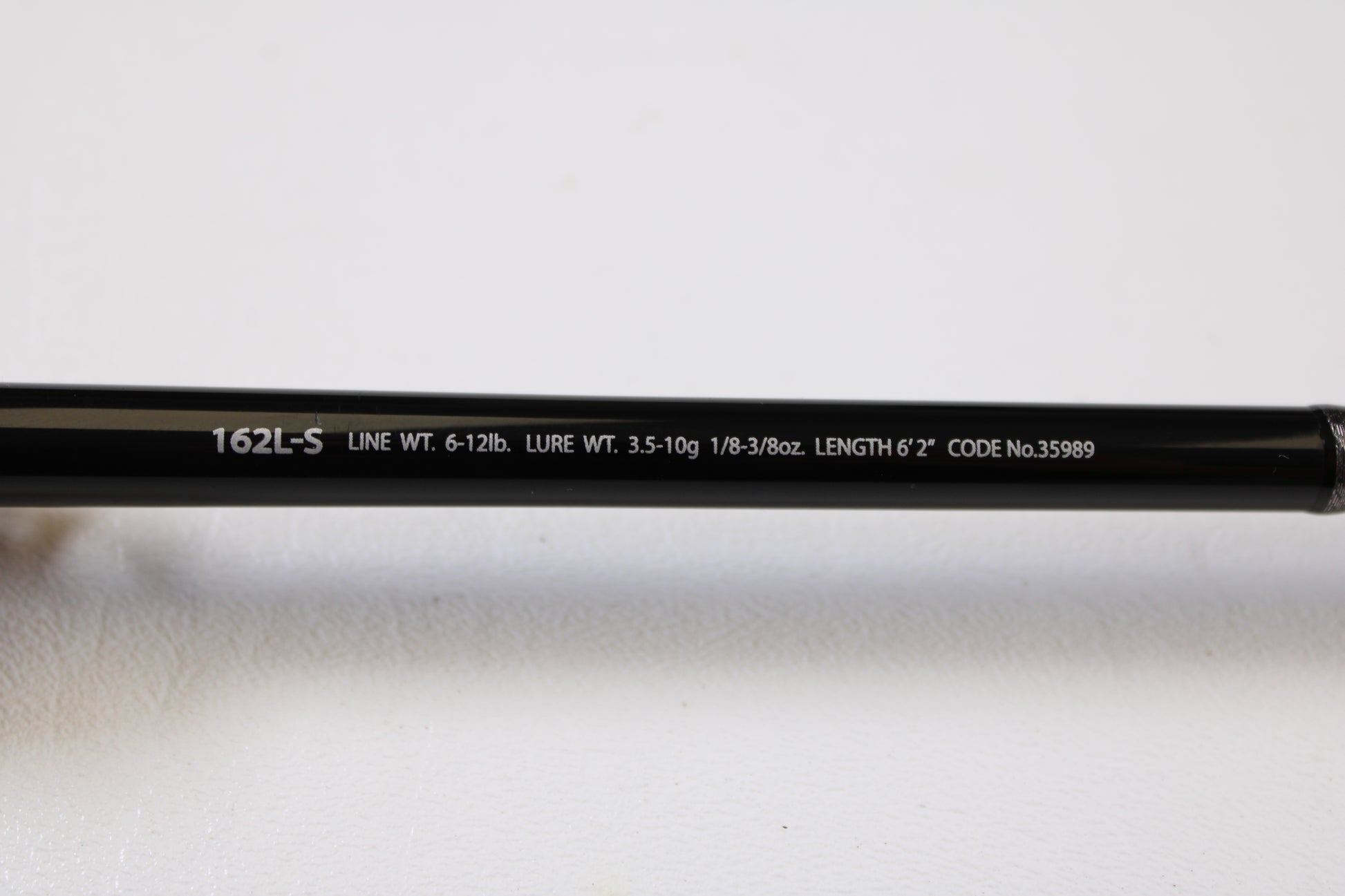 Close-up of text on Shimano Poison Ultima 162L-S 6'2" Light - Used Casting Rod (Very Good Condition): "162L-S LINE WT. 6-12lb. LURE WT. 3.5-10g LENGTH 6'2" CODE No.35989." Ideal for trade-in or your used Shimano collection. White background.
