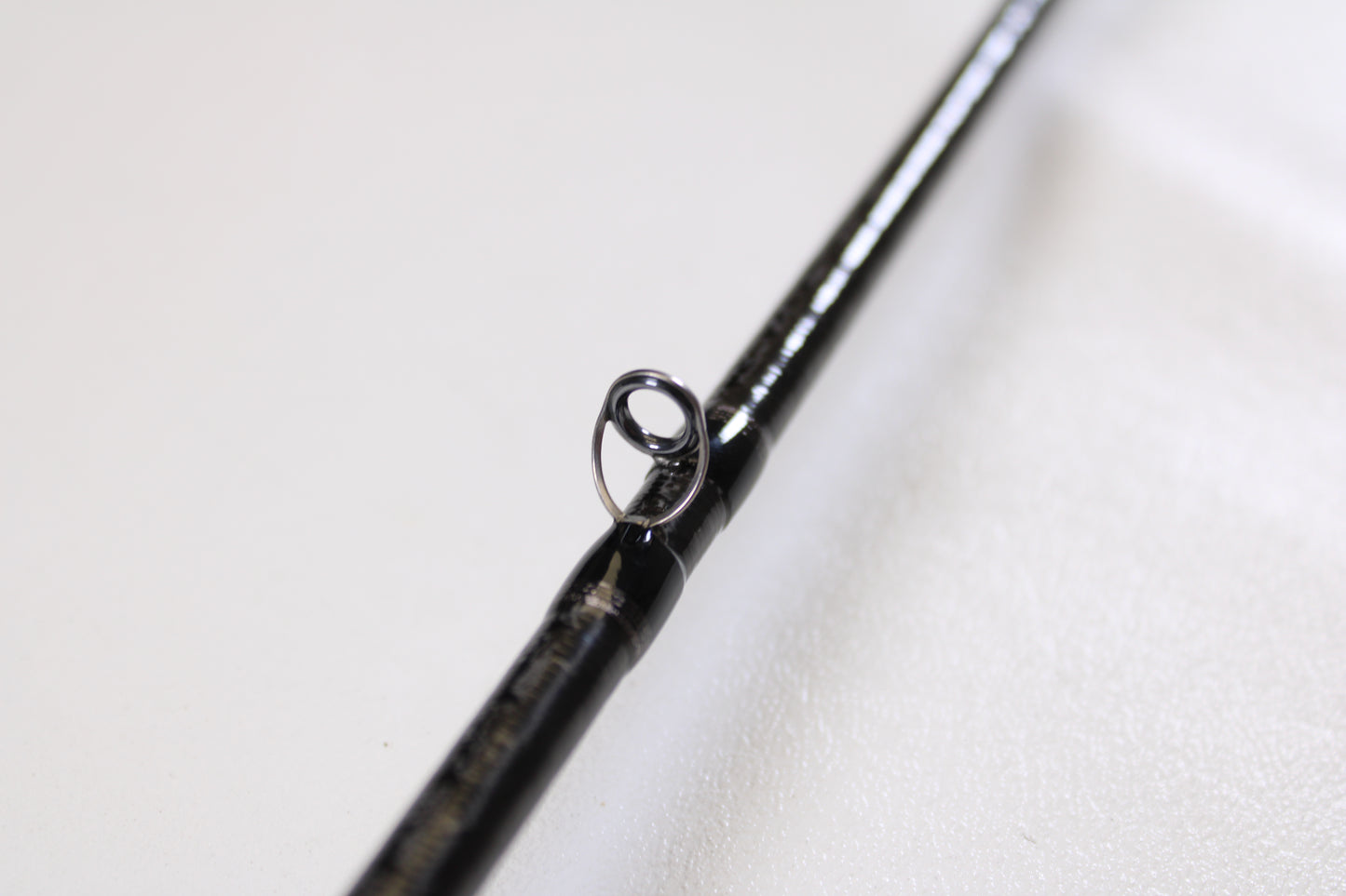 Close-up of a Shimano Poison Ultima 162L-S 6'2" Light - Used Casting Rod in very good condition, highlighting the metal guide ring against a white background. Trade in your used Shimano gear for store credit with our Rod and Reel Trade-In Program!.