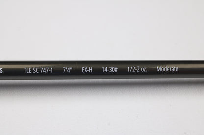 A close-up of a Temple Fork TFO Tactical Elite Bass TLE SC 747-1 7'4" Ex-Heavy used casting rod (excellent condition) shows its specs on the blank. This gear is part of our rod and reel trade-in program, displayed on a white background.