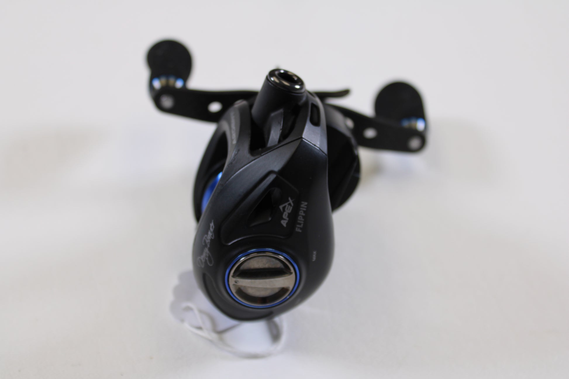 A close-up of the Ardent Denny Brauer Apex Flippin 6.5:1 LH Used Casting Reel in very good condition, shown on a white surface. Ideal for our Rod and Reel Trade-In Program—exchange your used gear for store credit. Handle and adjustment dial visible.