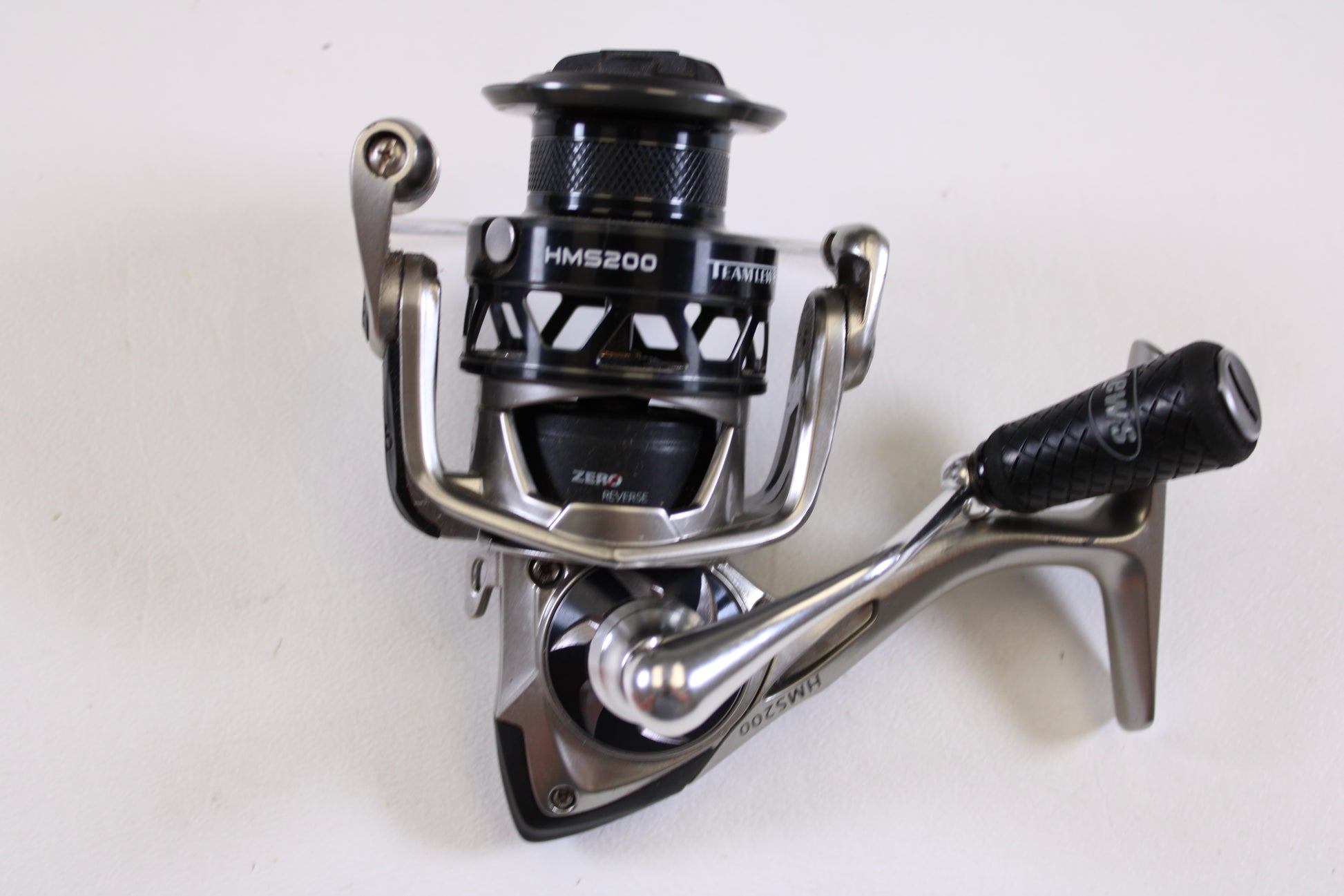 A close-up of a Lew's HyperMag HMS200 6.2:1 used spinning reel in fair condition (missing handle nut) is displayed on a white surface—ideal for upgrading via our rod and reel trade-in program for store credit on used gear.