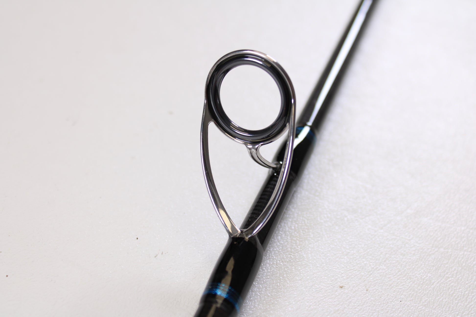 Close-up of the Tsunami Airwave Elite TSAWESS762LT 7'6" used spinning rod's guide, featuring a sturdy metal ring and frame on its black rod—ideal for anyone shopping quality pre-owned fishing gear.