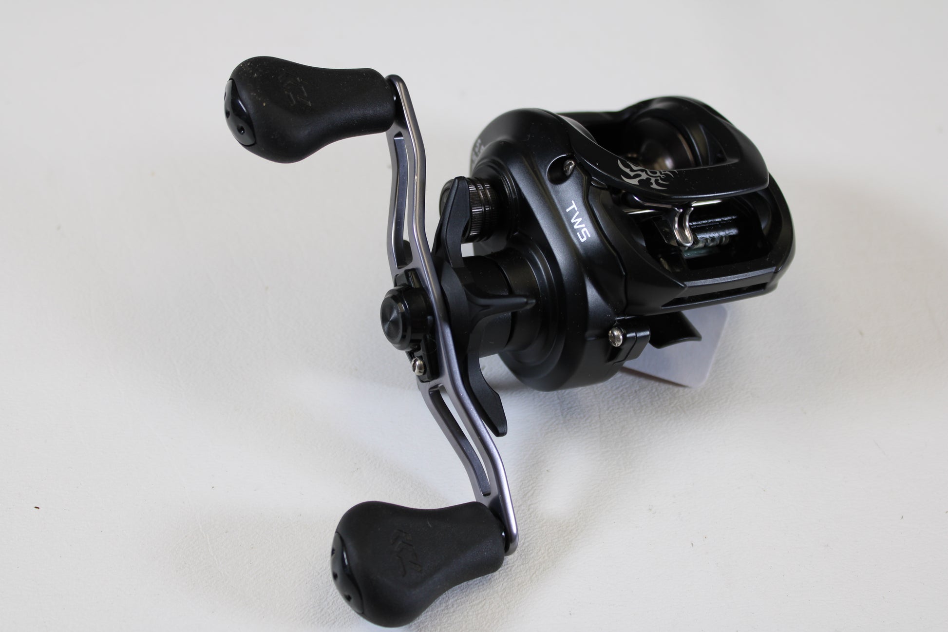 A Daiwa Tatula 150 TAT150P 5.5:1 RH used casting reel in excellent condition, with a sleek black dual-handle design, is perfect for trading in through our Rod and Reel Trade-In Program for store credit.