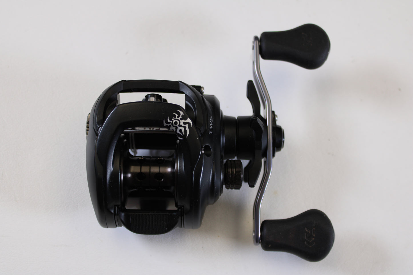 The Daiwa Tatula 150 TAT150P 5.5:1 RH - Used Casting Reel (Excellent Condition) is a black baitcasting reel with dual ergonomic handles and a silver crank—ideal for our Rod and Reel Trade-In Program if you're upgrading your gear.