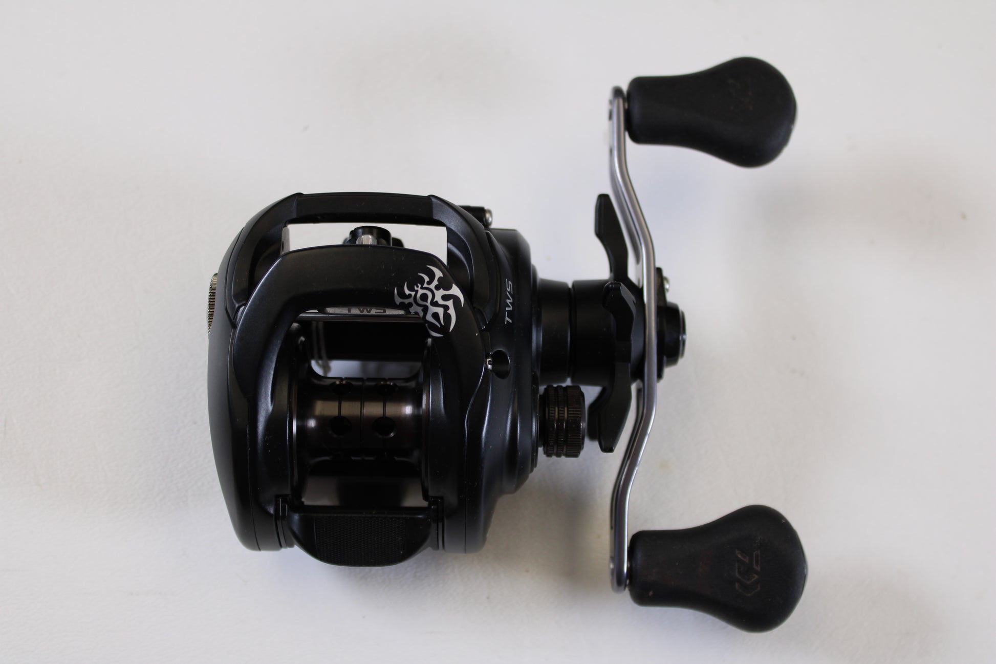 The Daiwa Tatula 150 TAT150P 5.5:1 RH - Used Casting Reel (Excellent Condition) is a black baitcasting reel with dual ergonomic handles and a silver crank—ideal for our Rod and Reel Trade-In Program if you're upgrading your gear.