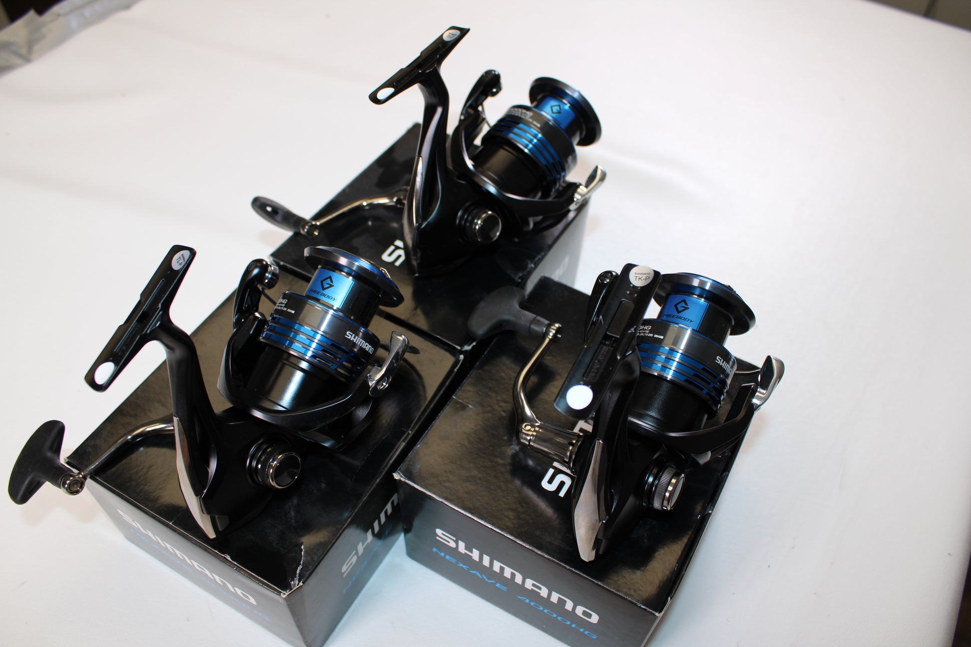 Three Shimano Nexave 4000HGFI spinning reels in mint condition are displayed atop their original boxes on a white surface.