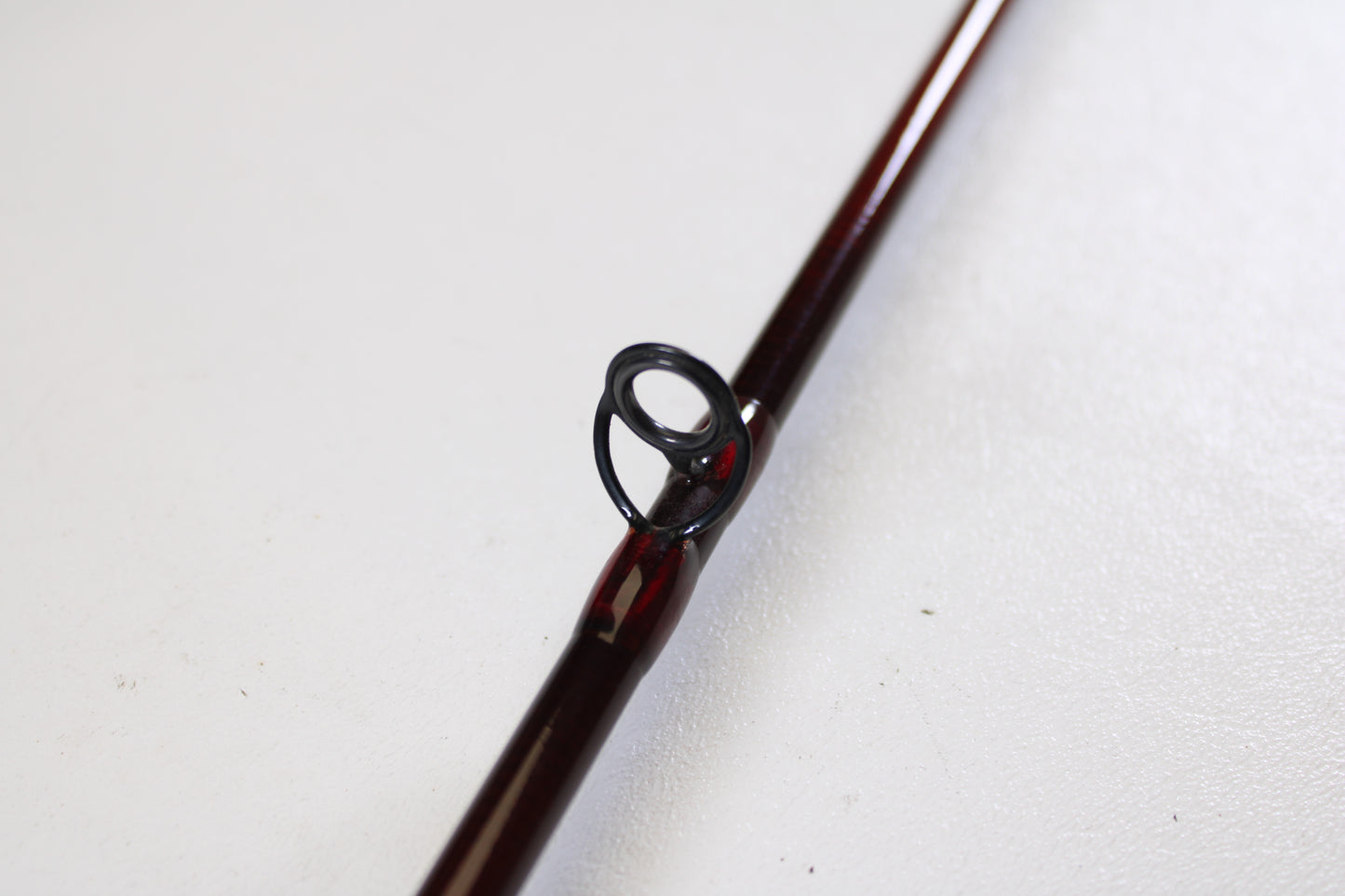 A close-up of the St. Croix Imperial I906.2 9'0" 6wt 2 Piece used fly rod in very good condition shows its dark metal guide on a brown rod—ideal for anglers seeking quality gear or exploring trade-in options, resting on a white textured surface.