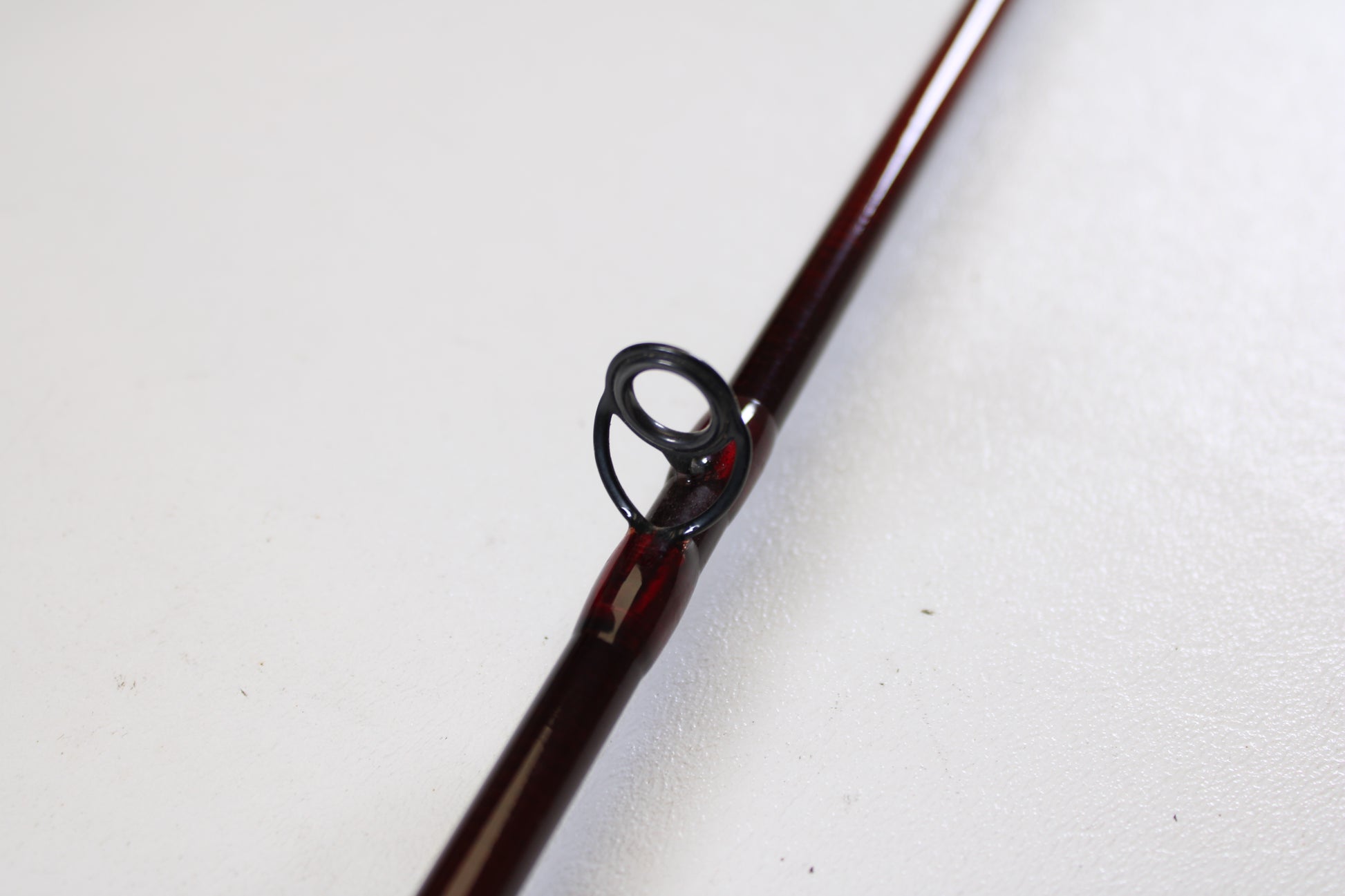 A close-up of the St. Croix Imperial I906.2 9'0" 6wt 2 Piece used fly rod in very good condition shows its dark metal guide on a brown rod—ideal for anglers seeking quality gear or exploring trade-in options, resting on a white textured surface.