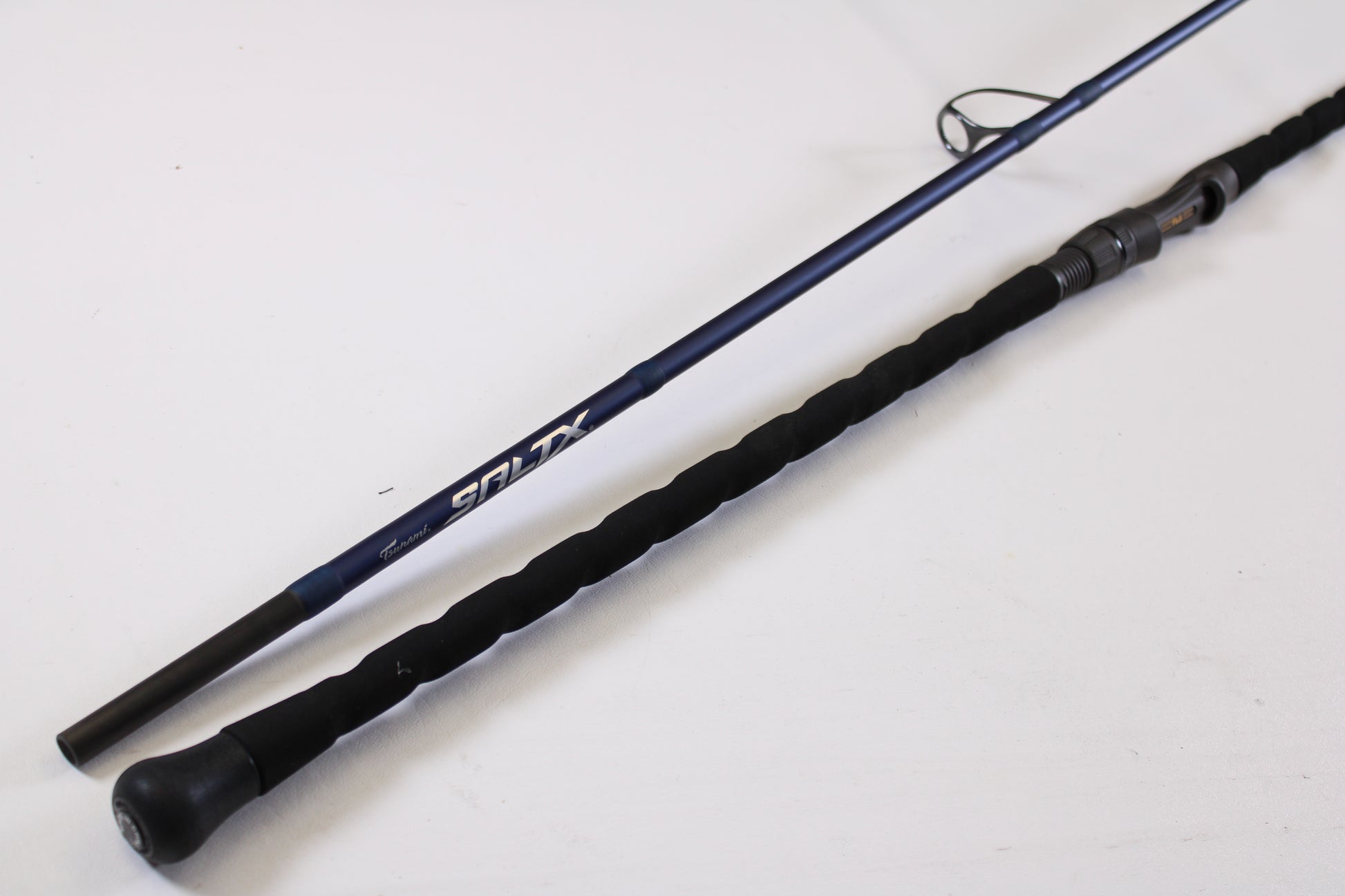 A close-up of the Tsunami SaltX Surf TSSTXIISS771M 7'7" Medium 1 Piece Used Spinning Rod in excellent condition, featuring a black foam handle and blue shaft—ideal for upgrading through our Rod and Reel Trade-In Program.