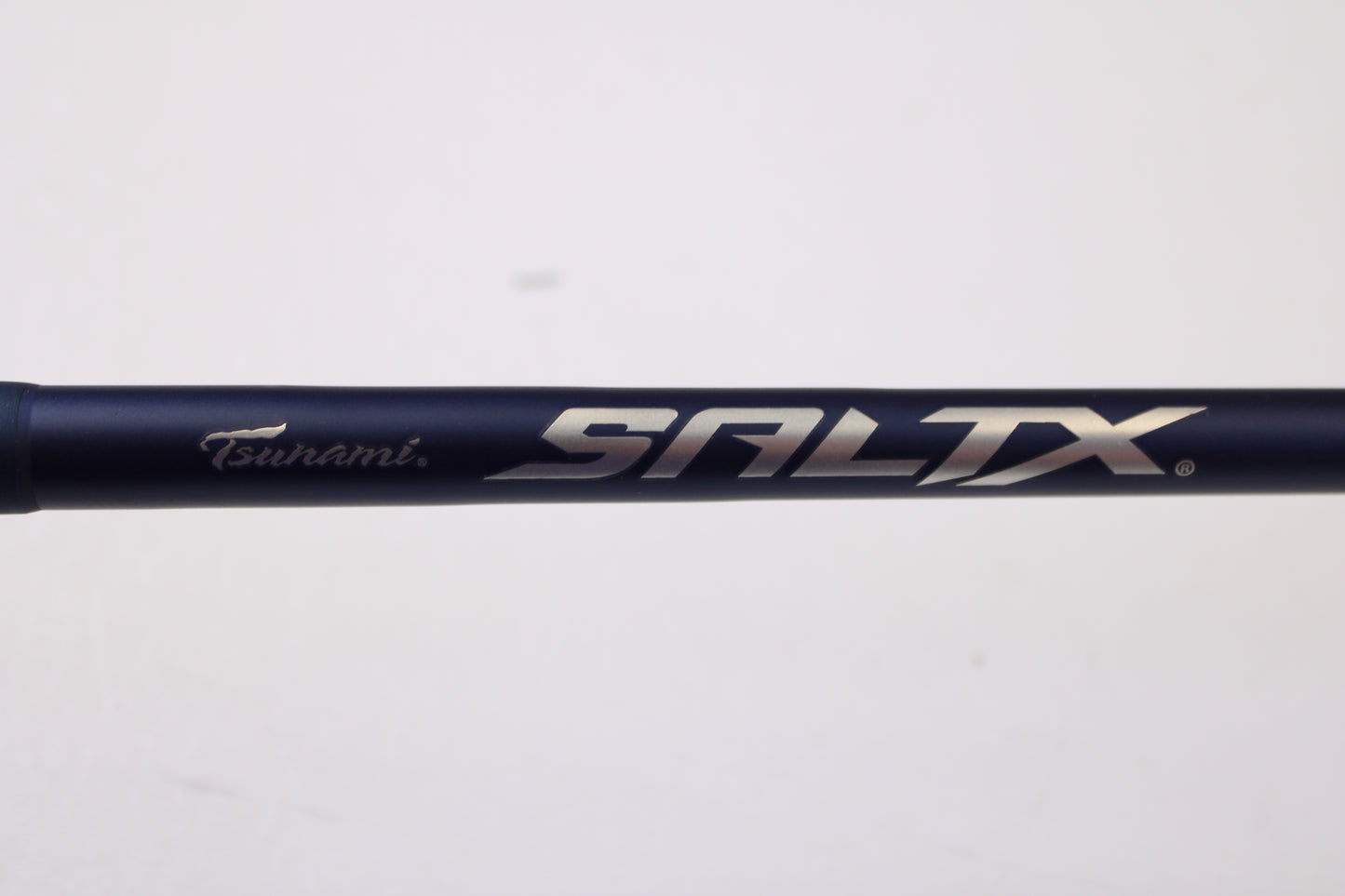 A close-up of the Tsunami SaltX Surf TSSTXIISS771M 7'7" Medium Used Spinning Rod in excellent condition, featuring the "Tsunami SALTX" logo on a dark blue finish—ideal for those exploring our Trade-In Program or quality used gear.