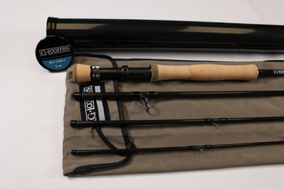 A G. Loomis NRX+ S 890-4 used fly rod in mint condition, black with a cork handle, is disassembled into four pieces on a gray cloth case beside a black rod tube and a round "G. Loomis" container.