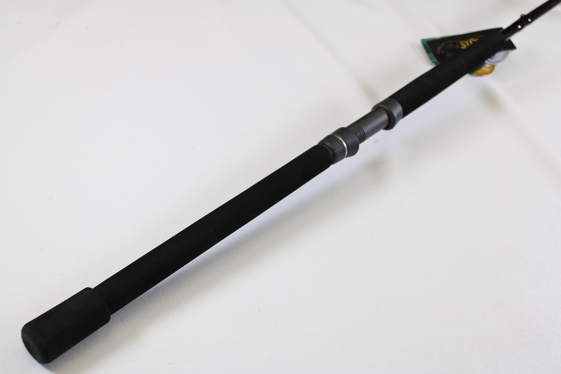 A close-up of a St. Croix Mojo Salt MSWC76MHMF 7'6" Medium Heavy used casting rod in mint condition shows its black foam handle on a white surface—perfect for those considering our Rod and Reel Trade-In Program.