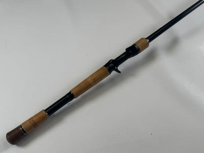 The Daiwa BLX BLXSG721HFB 7'2" Heavy casting rod, featuring a black handle and thick cork seal grips, is in excellent condition on a white surface. Ideal for stable casting with its trigger grip. Trade-in your used gear through our Rod and Reel Trade-In Program to earn store credit for an upgrade.
