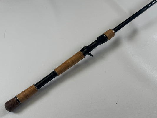 The Daiwa BLX BLXSG721HFB 7'2" Heavy casting rod, featuring a black handle and thick cork seal grips, is in excellent condition on a white surface. Ideal for stable casting with its trigger grip. Trade-in your used gear through our Rod and Reel Trade-In Program to earn store credit for an upgrade.