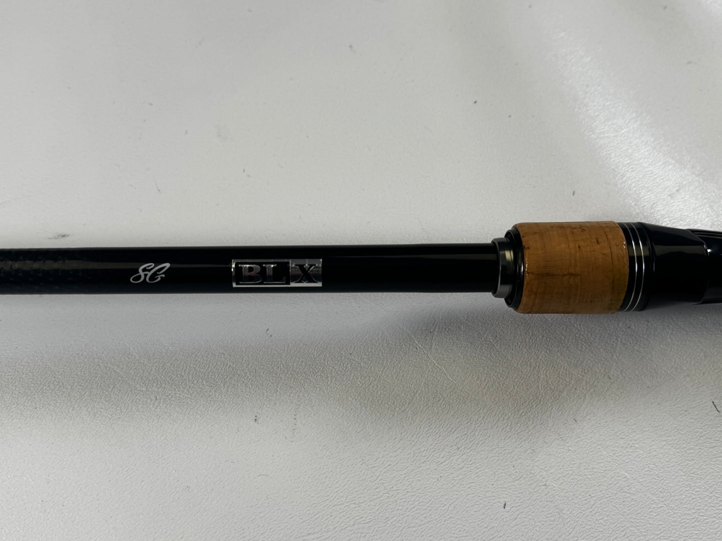 Close-up of a Daiwa BLXSG721HFB 7'2" Heavy casting rod handle with thick cork seal, black shaft, and "BLX" engraving. Ideal for upgrading through our Rod and Reel Trade-In Program. Shown against a smooth, light-colored background.