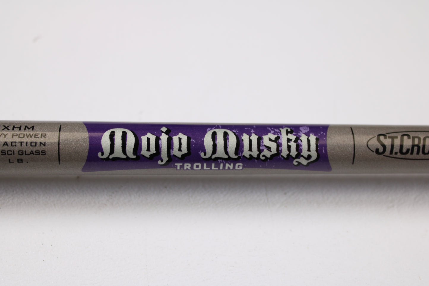 A close-up of a St. Croix Mojo Musky Trolling MMT70XHM 7'0" XH Used Casting Rod, mint condition, shows bold white lettering on purple. Trade in used gear like this for store credit with our Rod and Reel Trade-In Program; other logos are nearby.