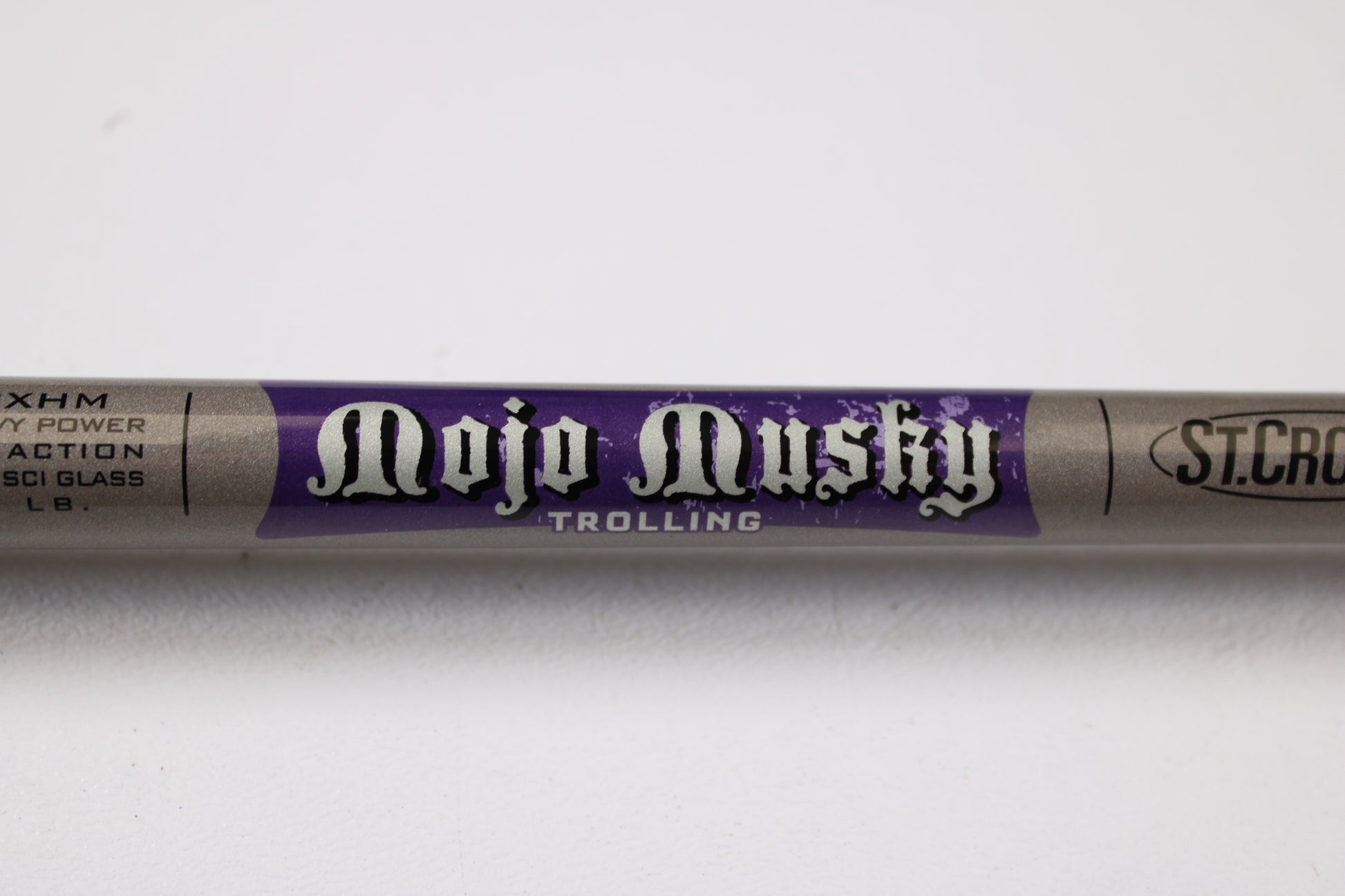 A close-up of a St. Croix Mojo Musky Trolling MMT70XHM 7'0" XH Used Casting Rod, mint condition, shows bold white lettering on purple. Trade in used gear like this for store credit with our Rod and Reel Trade-In Program; other logos are nearby.