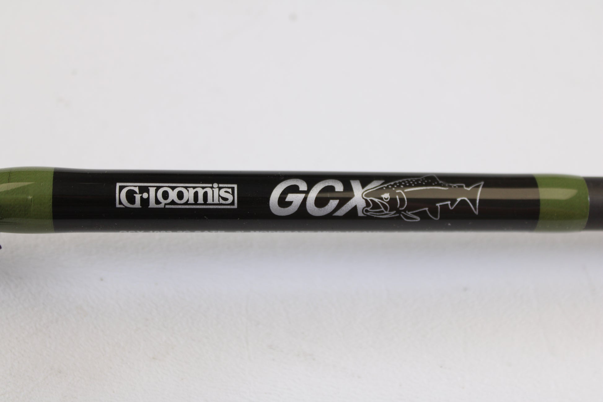 Close-up of a G. Loomis GCX Salmon 1083-2C SATR 9'0" Medium Heavy 2 Piece used casting rod in mint condition, featuring the brand logo and fish graphic—ideal for upgrades with our rod and reel trade-in program.