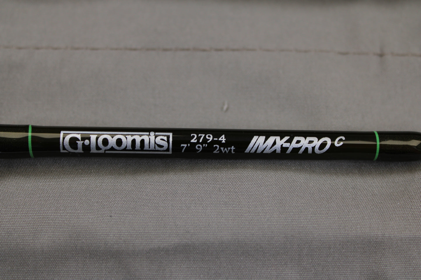 A close-up of a G. Loomis IMX-PRO Creek Fly Rod 279-4 7'9" #2 - Used Fly Rod - Mint Condition with white lettering on black, set against a gray fabric—ideal for anglers upgrading gear via our Rod and Reel Trade-In Program.