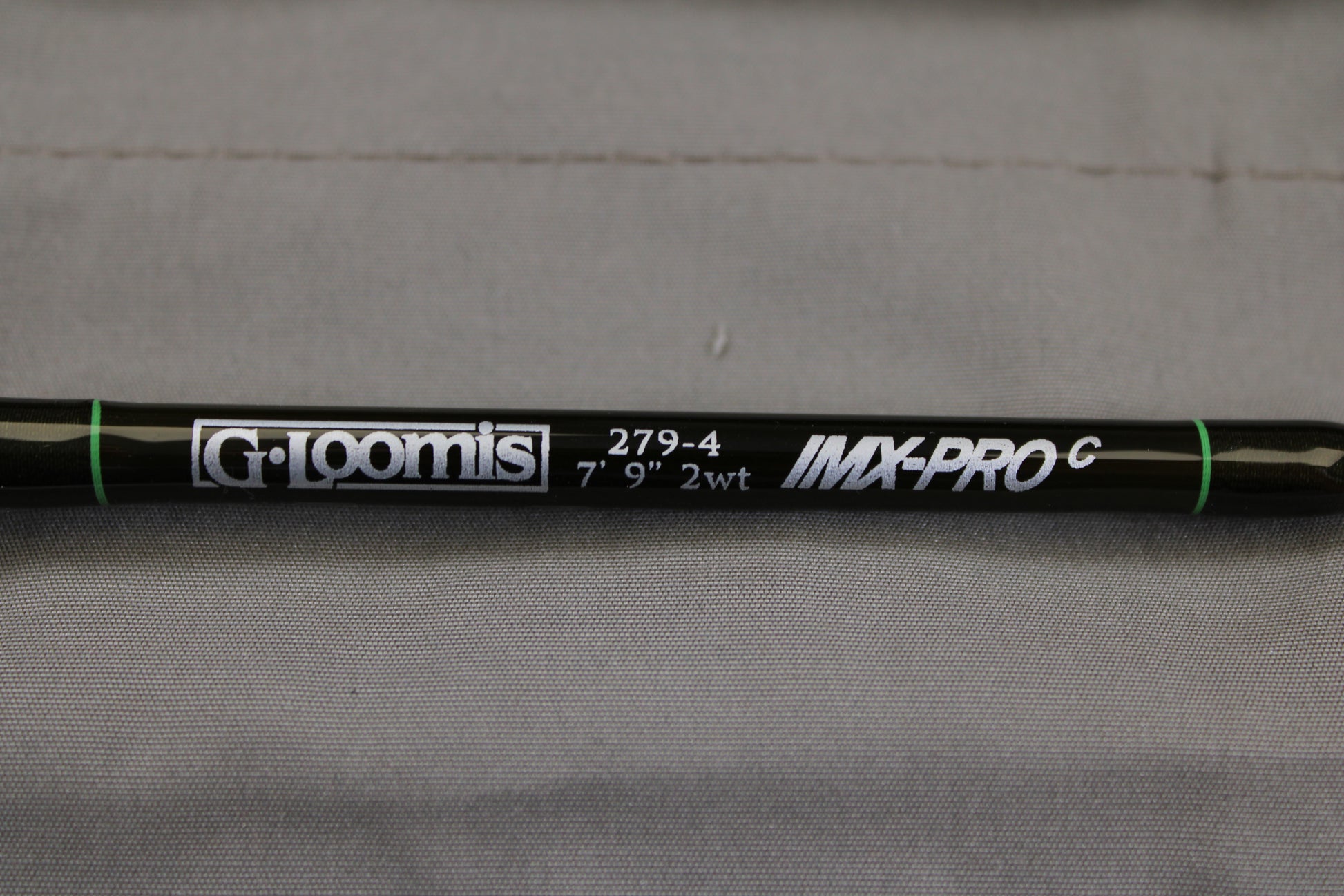 A close-up of a G. Loomis IMX-PRO Creek Fly Rod 279-4 7'9" #2 - Used Fly Rod - Mint Condition with white lettering on black, set against a gray fabric—ideal for anglers upgrading gear via our Rod and Reel Trade-In Program.