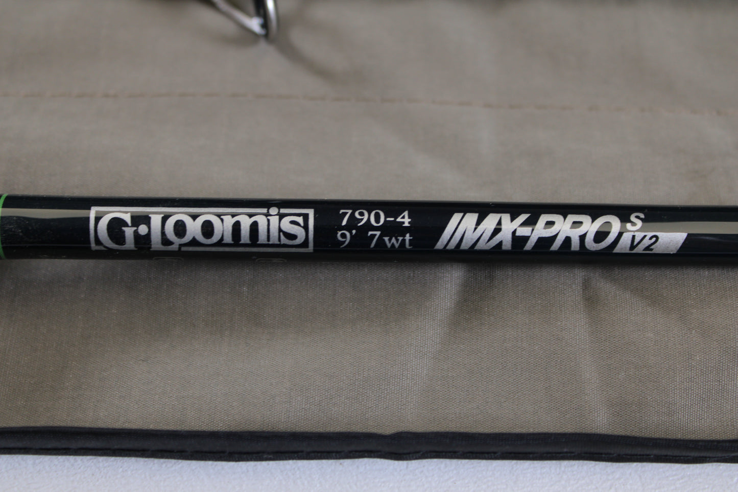 Close-up of a G. Loomis IMX-PRO V2S Saltwater 790-4 9'0" #7 used fly rod in mint condition on beige fabric—ideal for anglers looking to trade in or upgrade their gear for store credit.