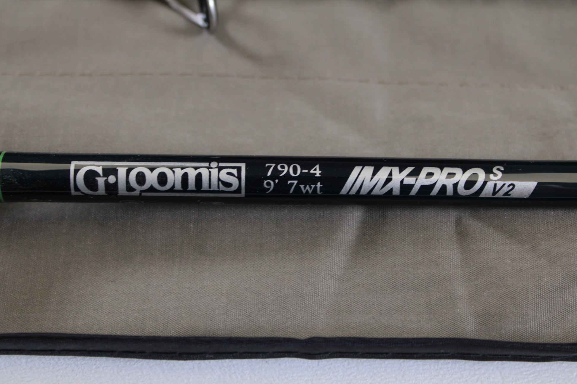 Close-up of a G. Loomis IMX-PRO V2S Saltwater 790-4 9'0" #7 used fly rod in mint condition on beige fabric—ideal for anglers looking to trade in or upgrade their gear for store credit.