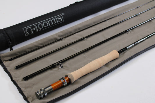 A G. Loomis IMX-PRO V2 Fly Rod 490-4 9'0" #4 in mint condition is displayed with a cork handle on a gray case beside a black G. Loomis tube—ideal for those considering our rod and reel trade-in program.