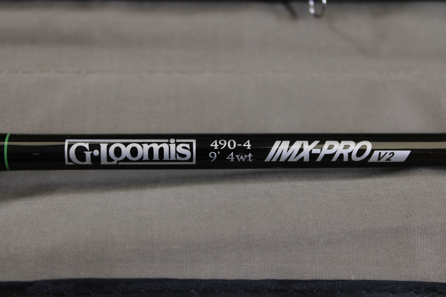 Close-up of a G. Loomis IMX-PRO V2 Fly Rod 490-4 9'0" #4 in mint condition, set against a neutral fabric background—a great choice for anglers considering our rod and reel trade-in program.