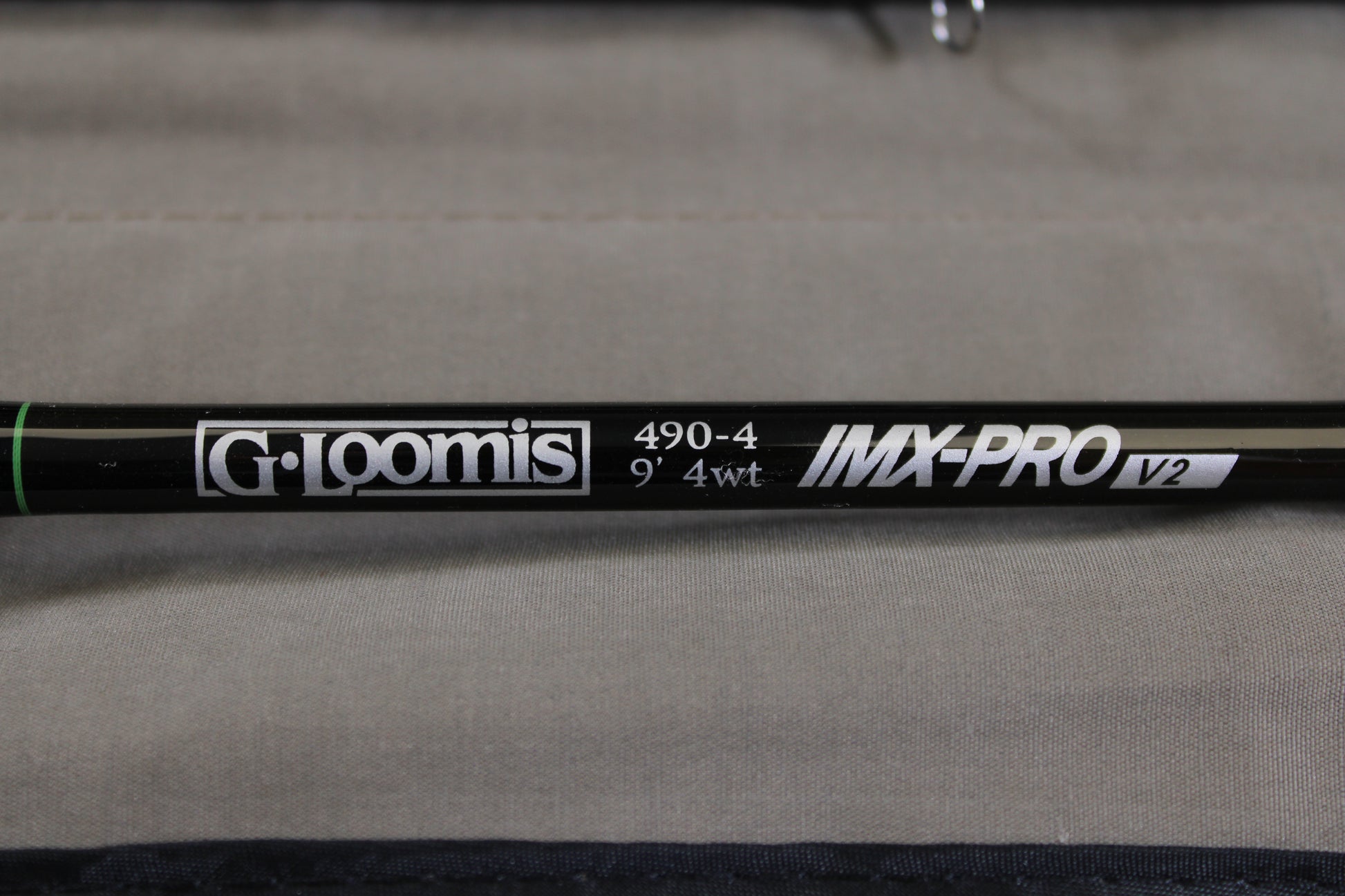 Close-up of a G. Loomis IMX-PRO V2 Fly Rod 490-4 9'0" #4 in mint condition, set against a neutral fabric background—a great choice for anglers considering our rod and reel trade-in program.