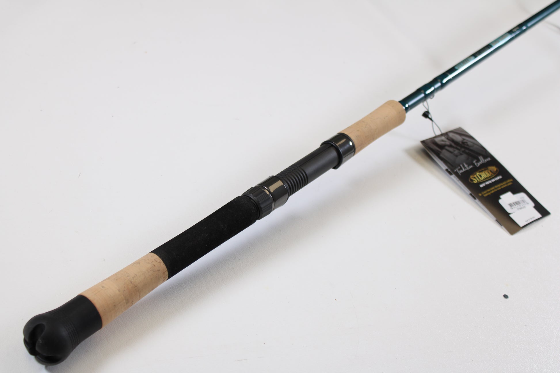 A St. Croix Mojo Inshore JIS66HF 6'6" Heavy used spinning rod in mint condition with a cork handle and black grip rests on a white surface. A tag shows it’s eligible for our Rod and Reel Trade-In Program for store credit.