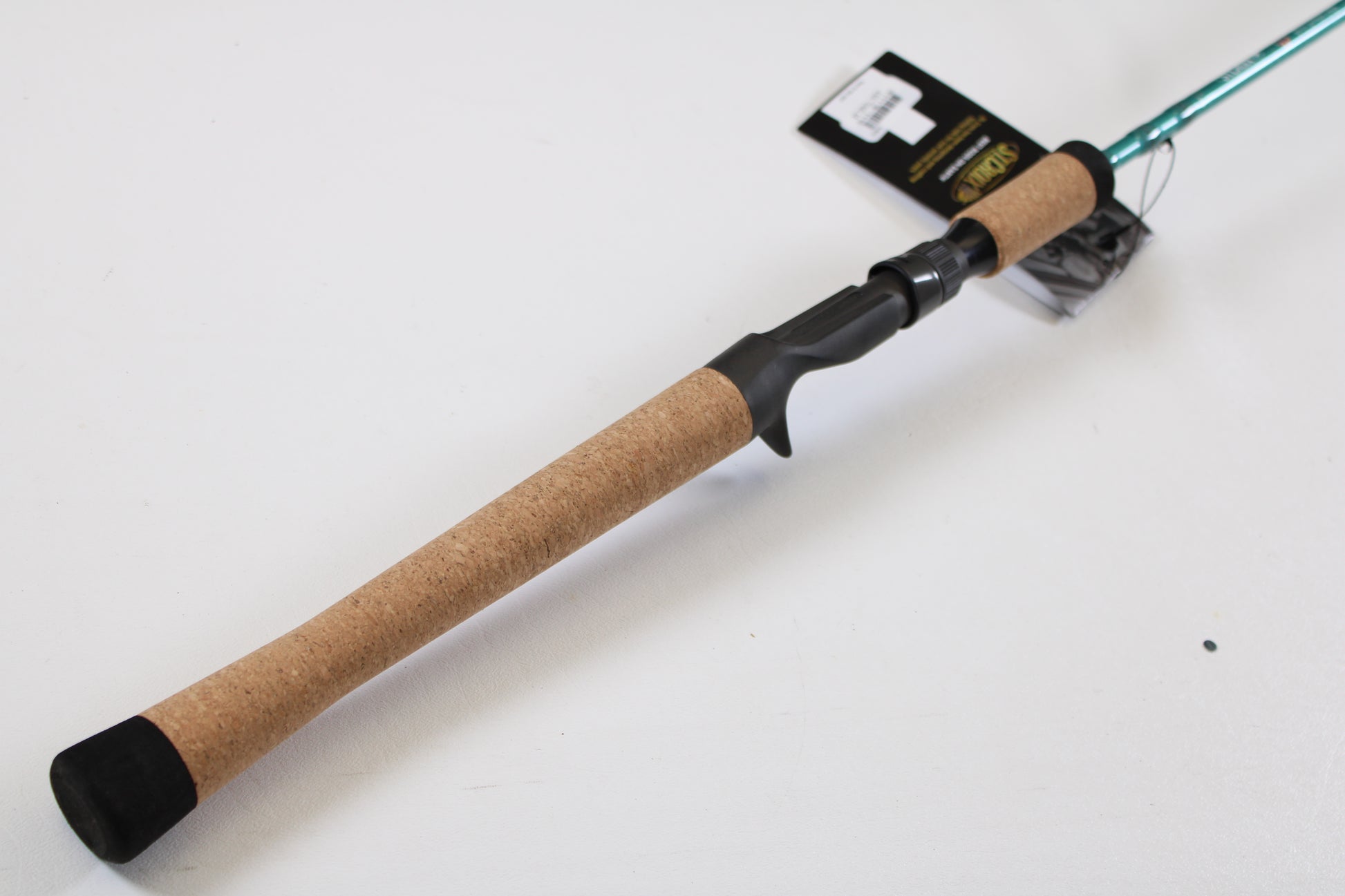 A close-up of the St. Croix Avid Inshore ASIC70MLM 7'0" Medium Light casting rod’s cork handle, black reel seat, and attached tag on a white background—ideal for those trading in used gear with our Rod and Reel Trade-In Program.