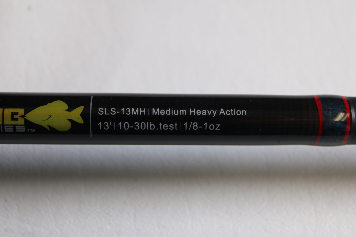 A close-up of the Falcon Slab Series SLS13MH 13'0" Medium Heavy 3pc Used Spinning Rod in excellent condition, showing its label on a black background with a yellow fish logo and red stripe—ideal for rod and reel trade-ins.