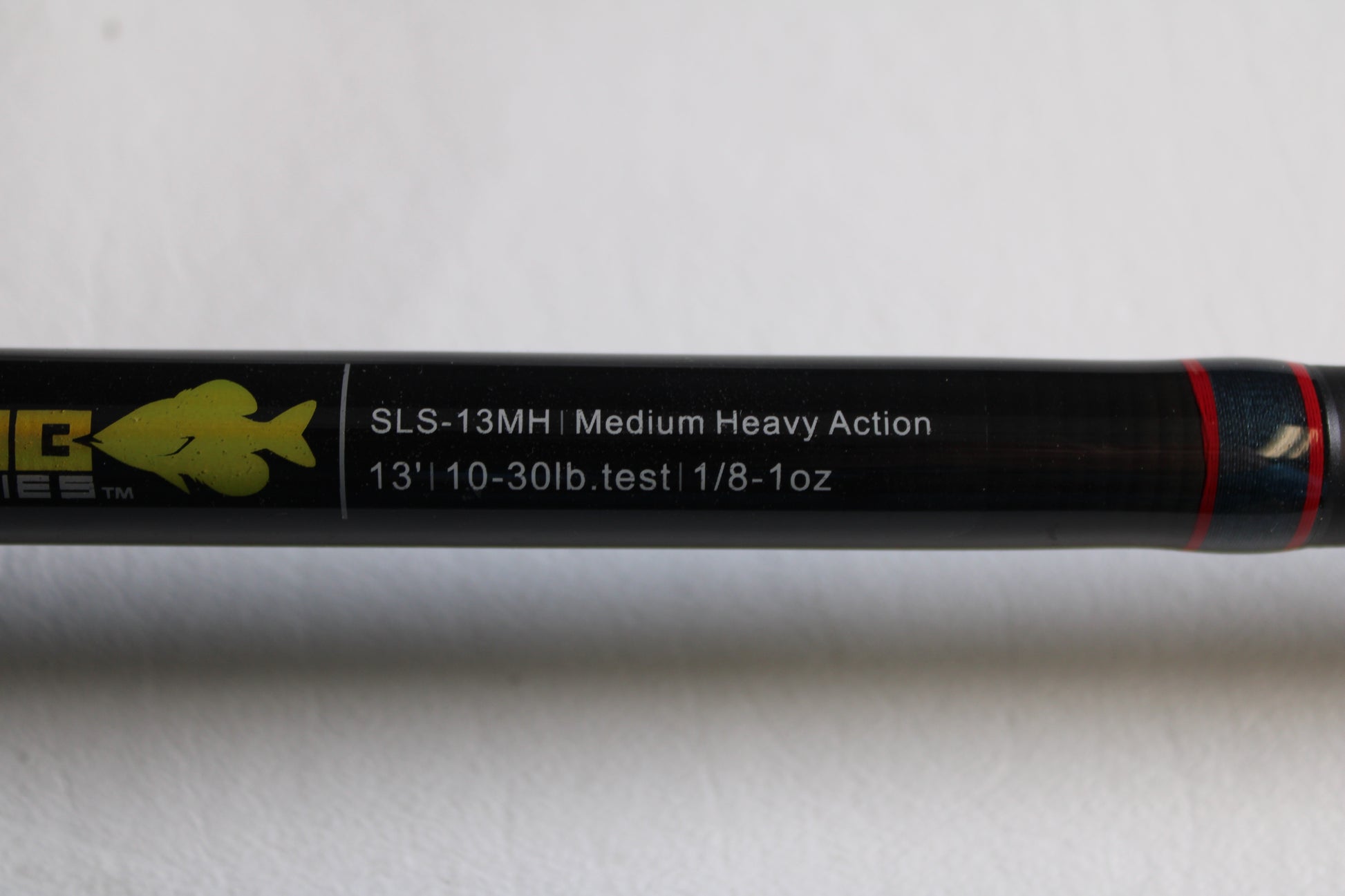 A close-up of the Falcon Slab Series SLS13MH 13'0" Medium Heavy 3pc Used Spinning Rod in excellent condition, showing its label on a black background with a yellow fish logo and red stripe—ideal for rod and reel trade-ins.