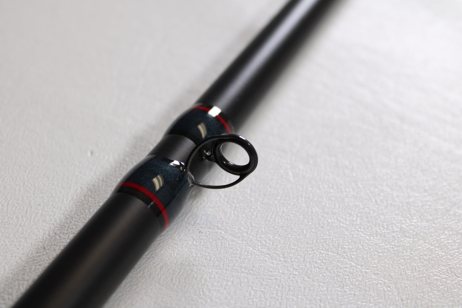 Close-up of the Falcon Slab Series SLS13MH 13'0" Medium Heavy 3pc Used Spinning Rod in excellent condition, with black finish, metal guide ring, and red-silver accents—ideal for used gear buyers or our rod and reel trade-in program.