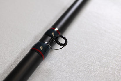 Close-up of the Falcon Slab Series SLS13MH 13'0" Medium Heavy 3pc Used Spinning Rod in excellent condition, with black finish, metal guide ring, and red-silver accents—ideal for used gear buyers or our rod and reel trade-in program.