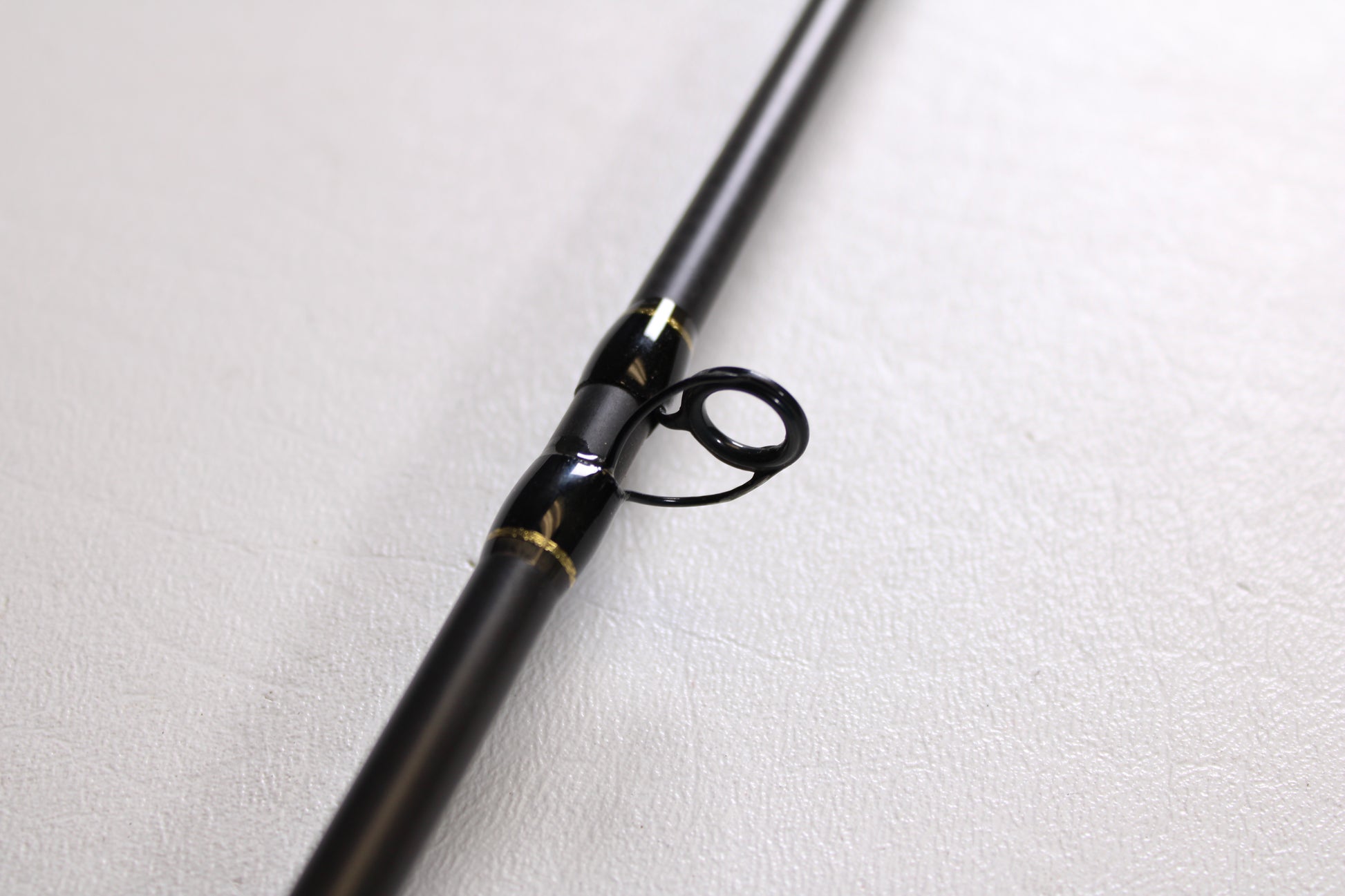 A close-up of the Falcon Cara T7 CC-4-166M 6'6" Medium used casting rod in very good condition, featuring a black body with metal line guide and gold accents—ideal for anyone seeking quality pre-owned Falcon gear.