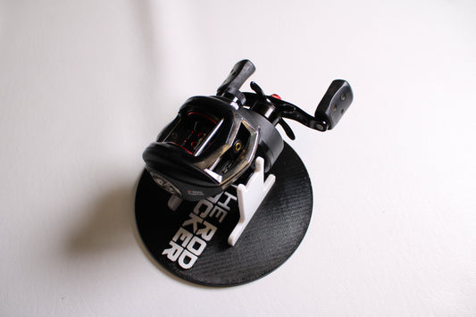 An Abu Garcia Revo 3 SX-L 6.4:1 used casting reel in good condition is displayed on a circular stand labeled "THE ROD RACKER" in white text, set against a plain white background.