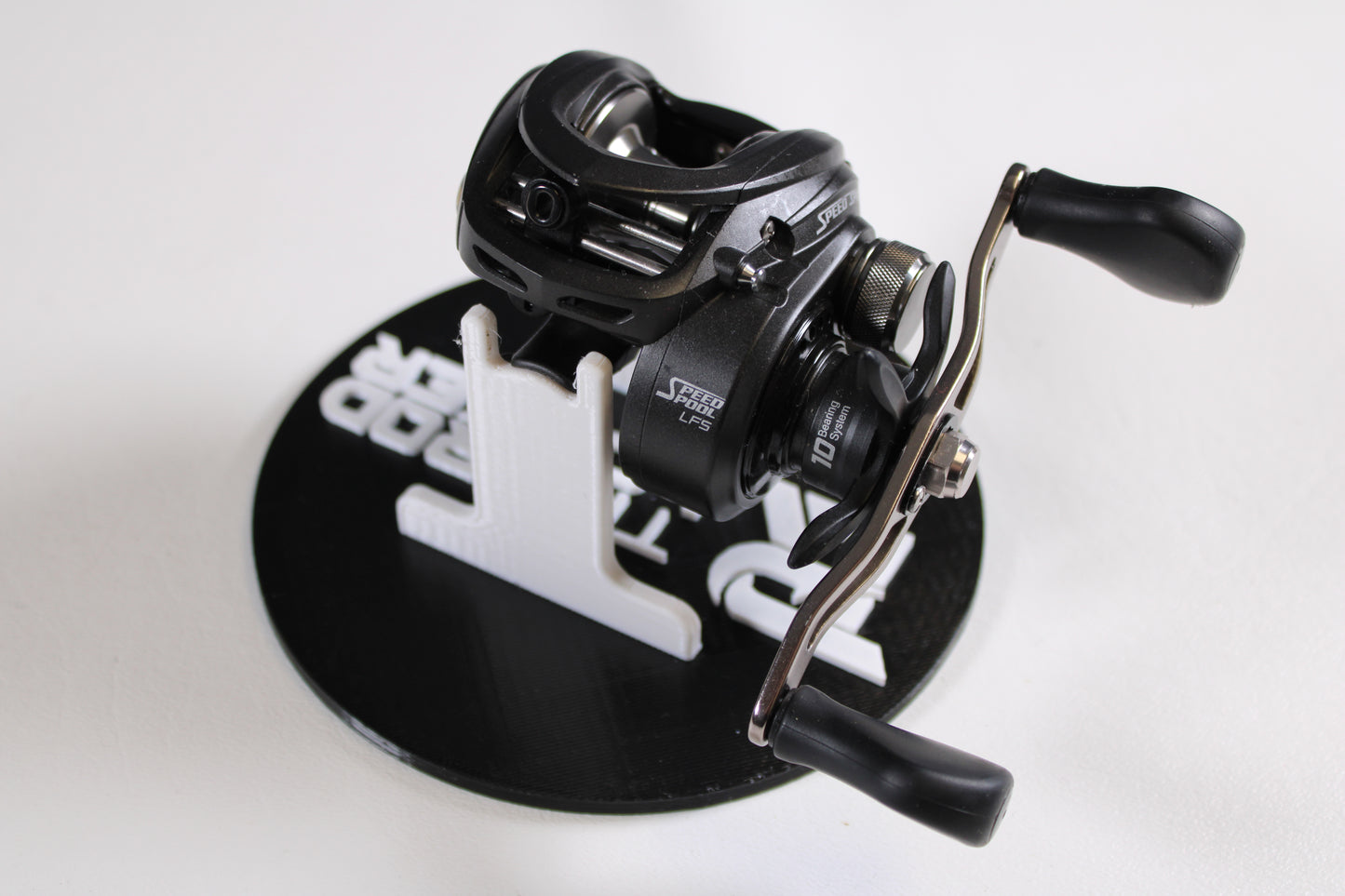 A Lew's Speed Spool SS1HLA 6.8:1 LH casting reel in very good used condition is shown with dual handles on a black and white circular stand, ideal for upgrading your gear or trading in through our Rod and Reel Trade-In Program.