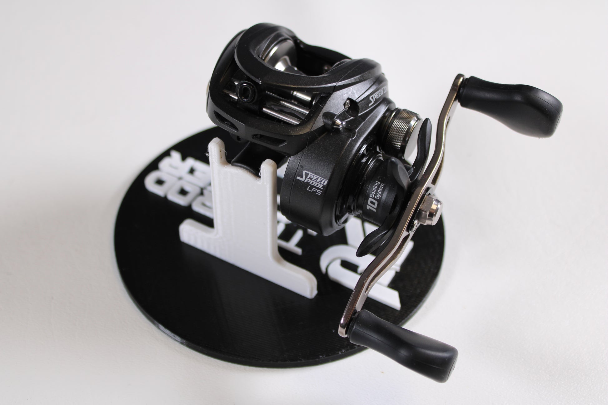 A Lew's Speed Spool SS1HLA 6.8:1 LH casting reel in very good used condition is shown with dual handles on a black and white circular stand, ideal for upgrading your gear or trading in through our Rod and Reel Trade-In Program.