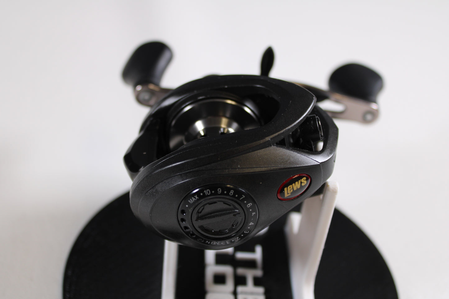A Lew's Speed Spool SS1HLA 6.8:1 LH used casting reel in very good condition is shown on a white stand with adjustment dials, handle grips, and the Lew's logo, featured as part of our Rod and Reel Trade-In Program.