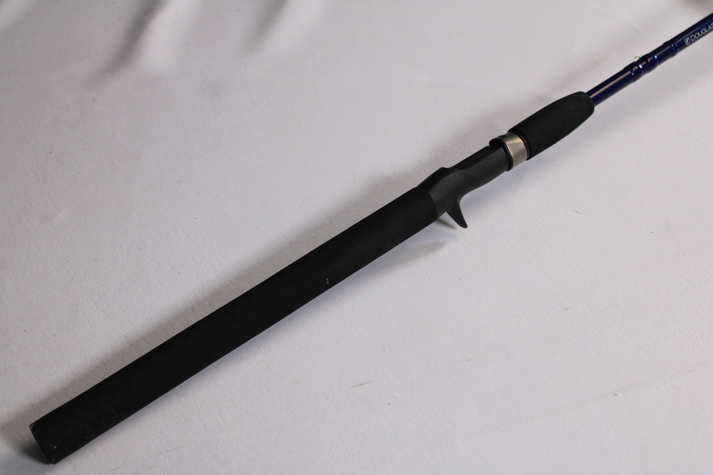 A close-up of a Douglas LRS LRSC784F 7'8" Medium used casting rod handle with trigger grip, lying on a white surface. Trade in gear like this for store credit through our rod and reel trade-in program. The rod extends out of frame to the right.
