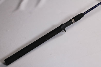 A close-up of a Douglas LRS LRSC784F 7'8" Medium used casting rod handle with trigger grip, lying on a white surface. Trade in gear like this for store credit through our rod and reel trade-in program. The rod extends out of frame to the right.