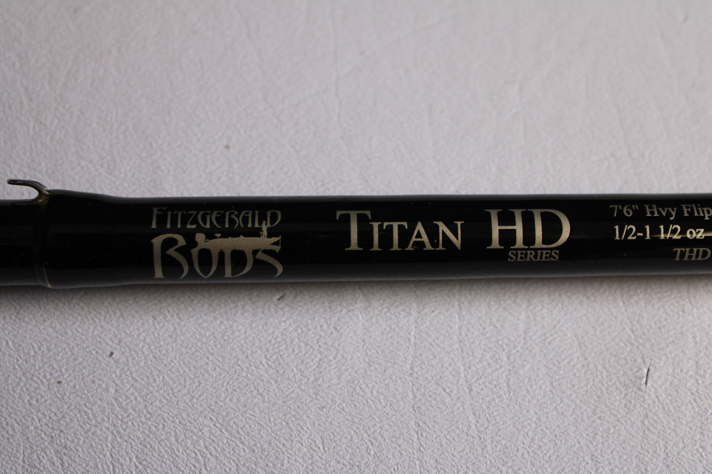 A close-up of a Fitzgerald Titan HD THD76H 7'6" Heavy Used Casting Rod (Very Good Condition) on a white textured background—ideal for our Rod and Reel Trade-In Program if you're upgrading your used gear.