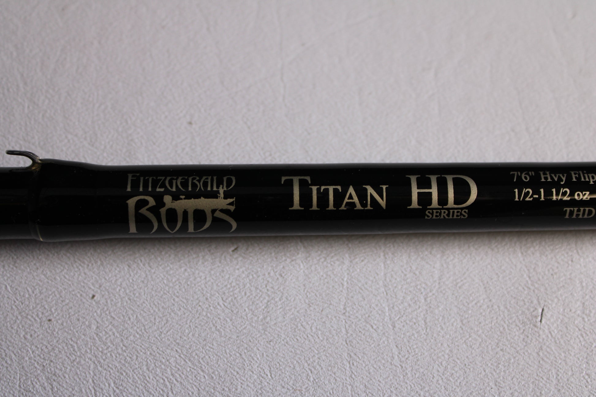 A close-up of a Fitzgerald Titan HD THD76H 7'6" Heavy Used Casting Rod (Very Good Condition) on a white textured background—ideal for our Rod and Reel Trade-In Program if you're upgrading your used gear.