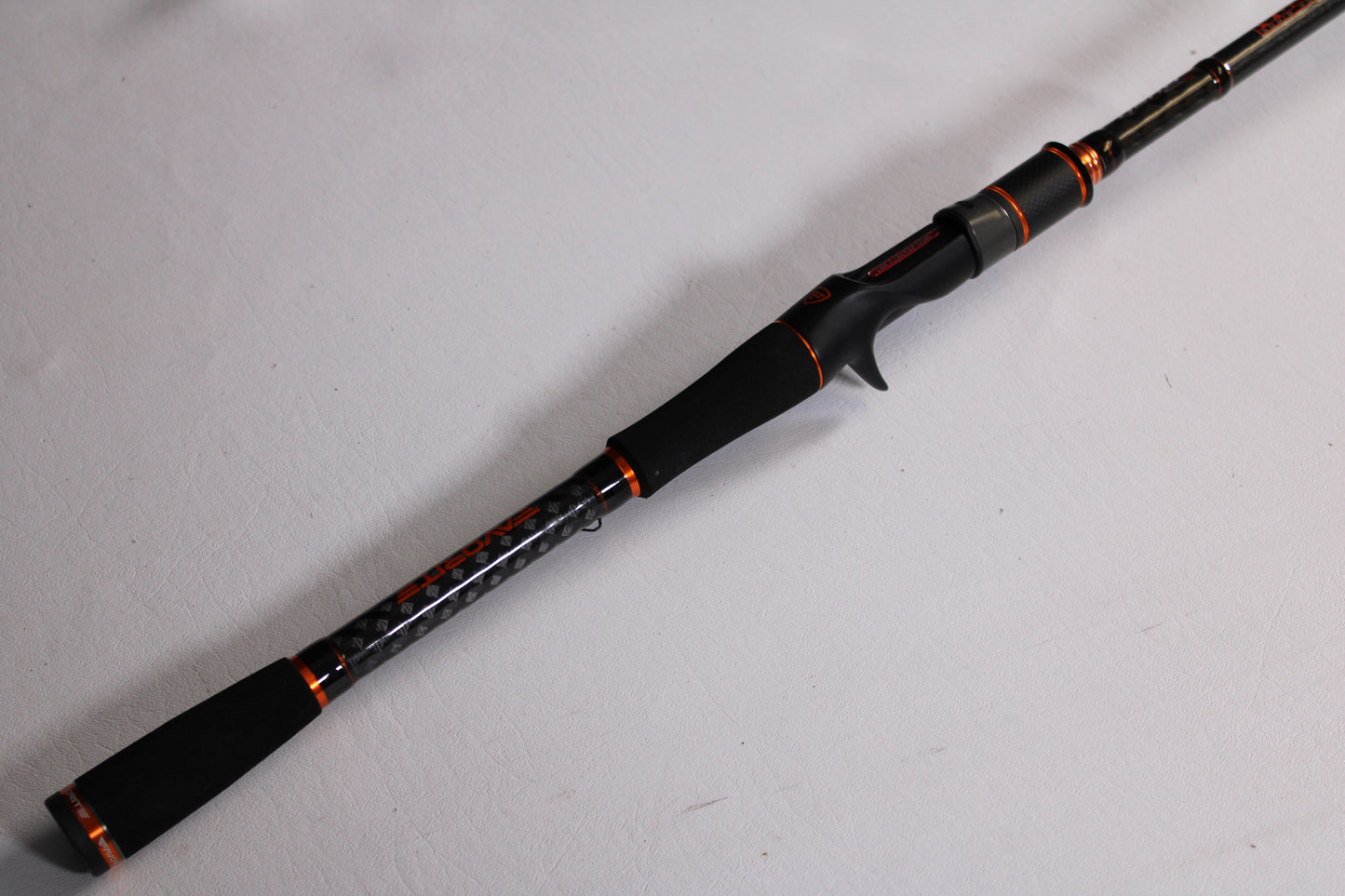 A close-up of the Favorite Fishing Rush Zach Birge RUHC-ZB-771H 7'7" Heavy Used Casting Rod—black and orange with a foam grip—shows it's in excellent condition, ideal for trading in through our Rod and Reel Trade-In Program for store credit.