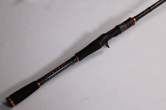 A close-up of the Favorite Fishing Rush Zach Birge RUHC-ZB-771H 7'7" Heavy Used Casting Rod—black and orange with a foam grip—shows it's in excellent condition, ideal for trading in through our Rod and Reel Trade-In Program for store credit.
