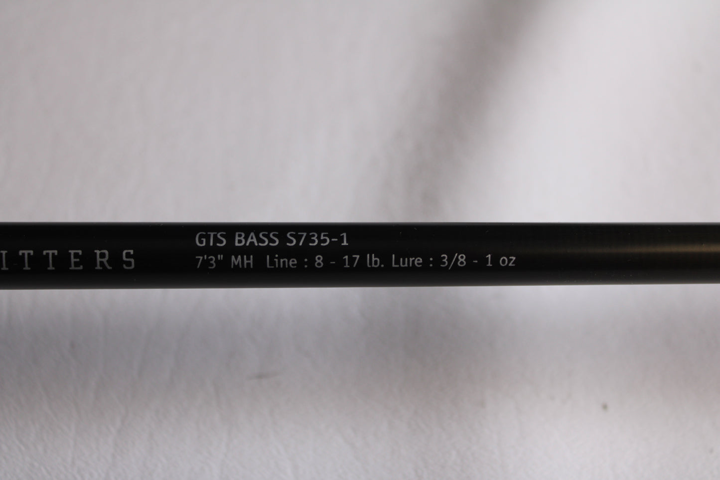 Close-up of a Temple Fork Outfitters GTS Bass S735-1 7'3" Medium Heavy used spinning rod in excellent condition, with white specs and partial promo text for our used gear and rod & reel trade-in program on a black background.
