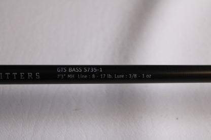 Close-up of a Temple Fork Outfitters GTS Bass S735-1 7'3" Medium Heavy used spinning rod in excellent condition, with white specs and partial promo text for our used gear and rod & reel trade-in program on a black background.