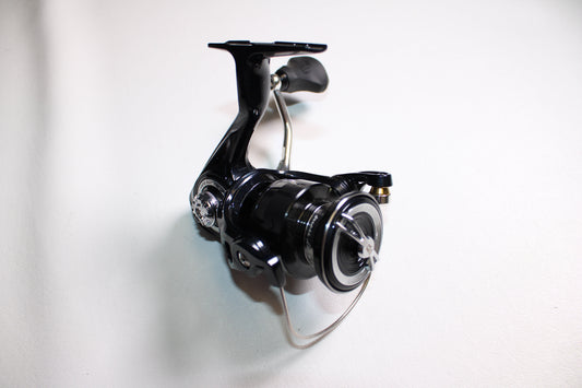 The 13 Fishing Aerios AE-6.2-1.0 Used Spinning Reel by 13 Fishing, in mint condition, is shown on a white surface with its handle, spool, and bail arm highlighted at an angle.